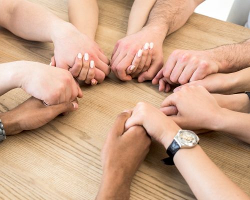 group-diverse-friends-holding-their-hands-together-wooden-table